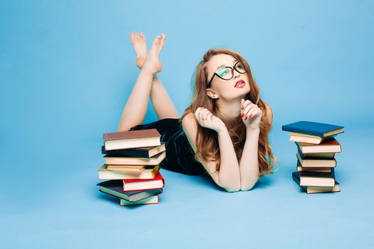 Sexy and beautiful female teacher in dress and eyeglasses, sitting on floor, posing and reading book, gesturing by hands, surprised looking up. Stylish pretty teacher or seductive female student.
