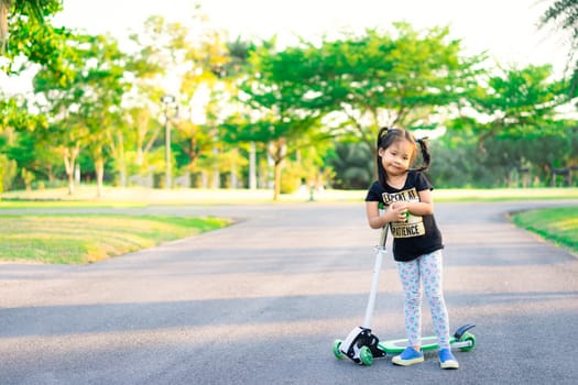 Cute little asian girl learning to ride a scooter in a park