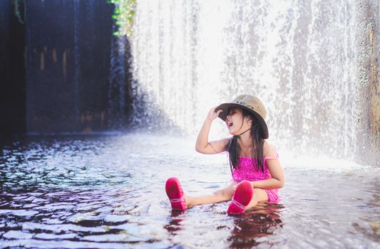 happy little asian girl wear hat playing waterfall on holiday