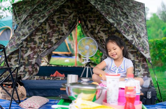 little girl sitting in front of tent while going camping.The concept of outdoor activities and adventures in nature.