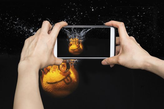 Taking pictures on mobile smart phone Smile orange with splashes of water on a black background