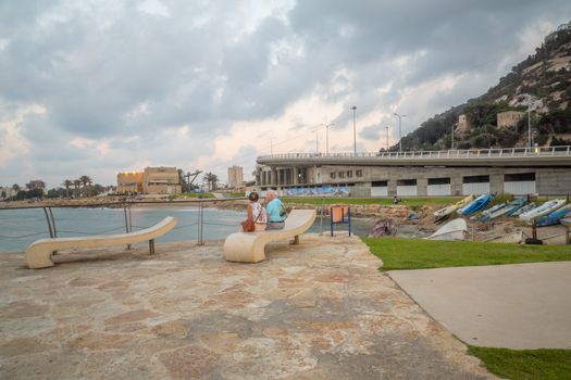 HAIFA, ISRAEL - AUGUST 06, 2018: Sunset beach scene with locals, boats, the Bat-Galim beach promenade and the Allenby Interchange, in Haifa, Israel