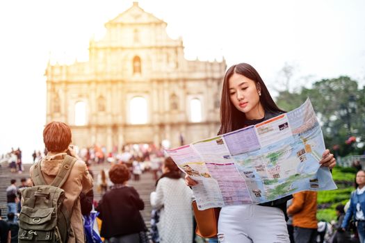MACAU - JANUARY 11, 2016: Young female tourist with map looking for a way to View of the Ruins of St. Paul's Cathedral in Macau. It is a popular tourist attraction of Asia.