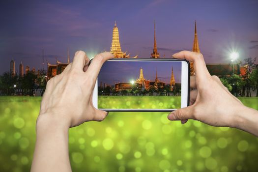 Taking pictures on mobile smart phone in Wat Phra Kaew (The Emerald Buddha) night view in Thailand 
