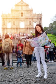 MACAU - JANUARY 11, 2016: Young female tourist with map looking for a way to View of the Ruins of St. Paul's Cathedral in Macau. It is a popular tourist attraction of Asia.