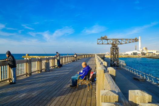 TEL-AVIV, ISRAEL - JANUARY 12, 2017: Scene with a restored crane, a commercial area, the Reading power station chimney, local fishermen and other visitors, in Tel-Aviv Port, Tel-Aviv, Israel