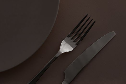 Empty plate and cutlery as mockup set on dark brown background, top tableware for chef table decor and menu branding design