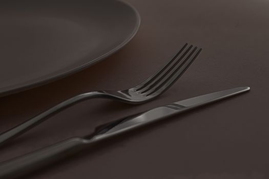 Empty plate and cutlery as mockup set on dark brown background, top tableware for chef table decor and menu branding design