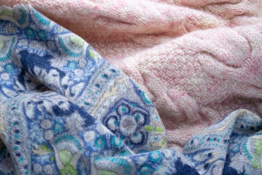 Soft folds of a warm pink knitted woolen pullover and a blue decorated scarf to be used as background