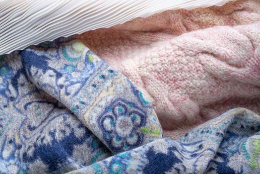 Soft folds of a warm pink knitted woolen pullover and a blue decorated scarf with a white pleated foulard to be used as background