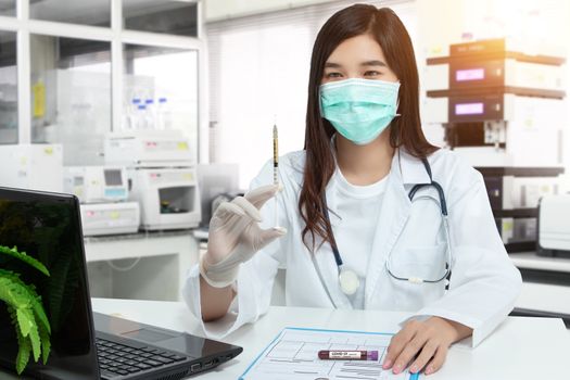 Asian doctor holds a syringe, blood sample test tube for covid-19 analyzing with patient file on desk in lab. laboratory analyzing for testing and invent drug and vaccine during Coronavirus epidemic