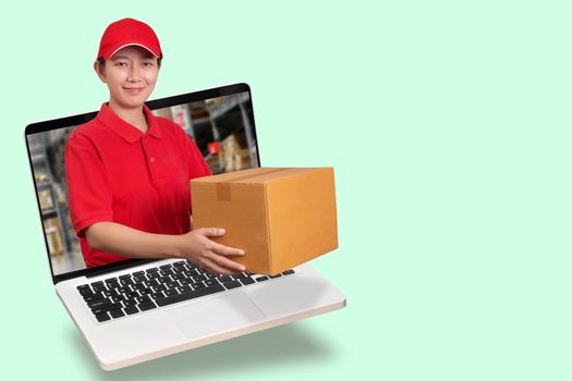 Asian delivery woman in red shirt with blur warehouse background, holding goods order in package parcel out from laptop computer isolated with copy space. order online and delivery service concept