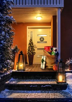 Welcome Christmas - house entrance snowy steps and door with decoration. Santas present sack with gift boxes