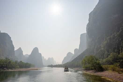 Boat on Li river cruise and karst formation mountain landscape in the fog between Guiling and Yangshuo, Guangxi province, China