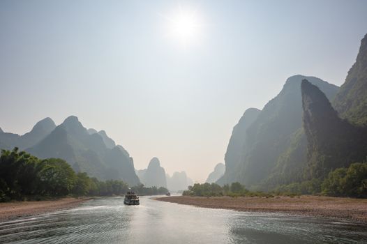 Boat on Li river cruise and karst formation mountain landscape in the fog between Guiling and Yangshuo, Guangxi province, China