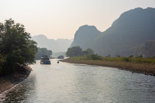 Boat on Li river cruise and karst formation mountain landscape in the fog between Guiling and Yangshuo, Guangxi province, China