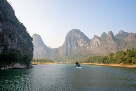 Boat on Li river cruise and karst formation mountain landscape in the fog between Guiling and Yangshuo, Guangxi province, China