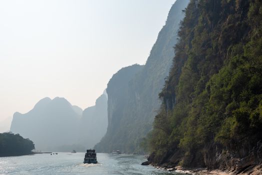 Boat on Li river cruise and karst formation mountain landscape in the fog between Guiling and Yangshuo, Guangxi province, China