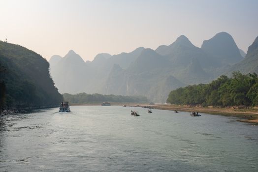 Boat on Li river cruise and karst formation mountain landscape in the fog between Guiling and Yangshuo, Guangxi province, China