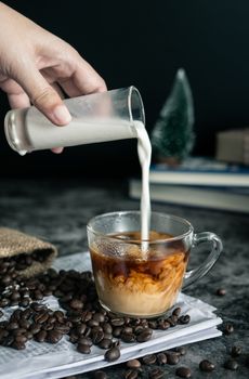 barista making latte. hand pouring milk into a cup of espresso coffee, preparing coffee drink. vertical image, cropped shot