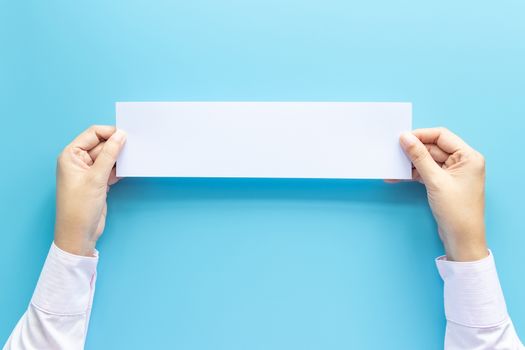 close up hands holding empty white blank horizontal paper for flyer or invitation mock up isolated on a blue background.