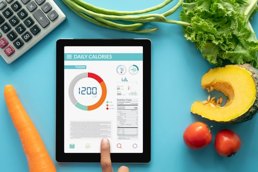 Calories counting , diet , food control and weight loss concept. woman using Calorie counter application on tablet at dining table with fresh vegetable and calculator