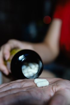 Two white capsules in a woman's hand while sitting on the bed