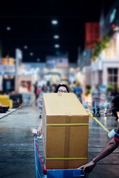 Asian woman feeling happy when her purchase a big product with cartons in shopping cart in department store or exhibit hall expo