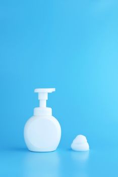 plastic pump bottle and mousse foam or cleansing foam isolated on blue background, vertical with copy space. cleaning concept