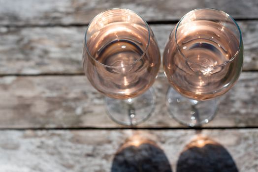 Two glasses of rose wine on a wooden table in sunlight top view