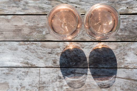 Two glasses of rose wine on a wooden table in sunlight top view