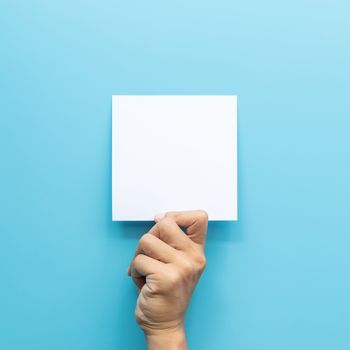 man hand holding blank card paper sheet isolated on blue background with copy space.