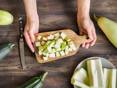 Zucchini harvest. Woman slices zucchini cubes for freezing on wooden table. Farm organic zucchini harvesting Top view or flat lay.