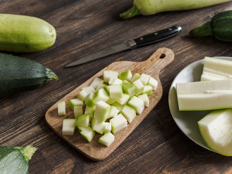 Zucchini harvest. Slices farm organic zucchini cubes for freezing on woodencutting board over brown wooden table. Zucchini harvesting concept.