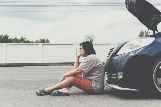 Asian woman 40s alone driver checking a car engine for fix and repair problem with unhappy and dismal between waiting a car mechanic from car engine problem at roadside