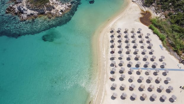 Aerial day top view of Sithonia Chalkidiki peninsula with crystal clear waters & sea beds with umbrellas next to small rocky island.