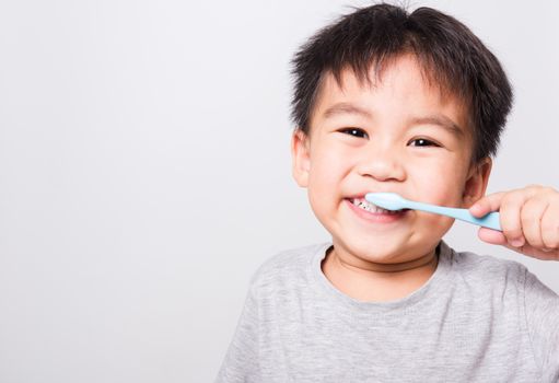 Closeup Asian face, Little children boy hand holds toothbrush he brushing teeth myself on white background with copy space, health medical care