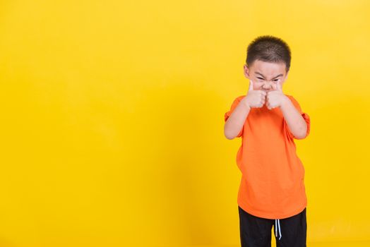 Asian Thai happy portrait cute little cheerful child boy wearing an orange t-shirt looking camera, studio shot isolated on yellow background with copy space