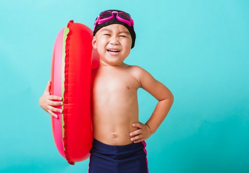 Summer vacation concept, Portrait Asian happy cute little child boy wear goggles and swimsuit hold watermelon inflatable ring, Kid having fun on summer vacation, studio shot isolated blue background