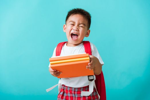 Back to school. Portrait Asian happy funny cute little child boy smiling and laugh holding books, studio shot isolated blue background. Kid from preschool kindergarten with school bag education