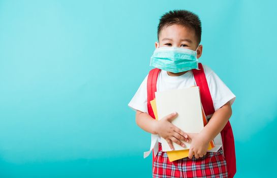 Back to school coronavirus Covid-19 education. Portrait Asian little child boy kindergarten wear face mask protective and school bag hold book before going to school, studio shot isolated background