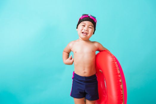 Summer vacation concept, Portrait Asian happy cute little child boy wear goggles and swimsuit hold watermelon inflatable ring, Kid having fun on summer vacation, studio shot isolated blue background