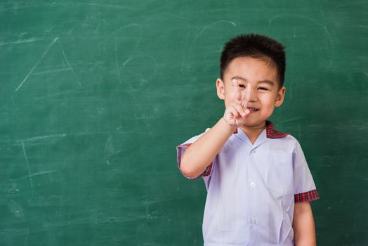 Back to School. Happy Asian funny cute little child boy from kindergarten in student uniform show finger V-sign smiling on green school blackboard, First time to school education concept, studio shot