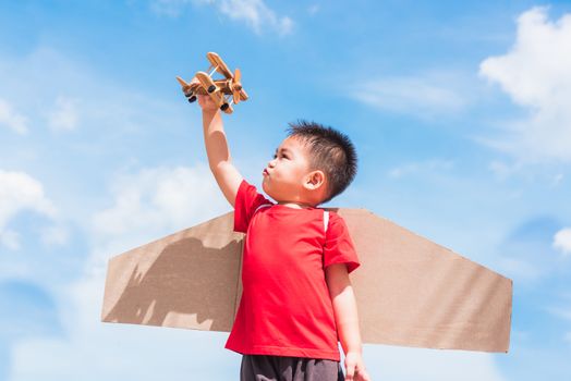 Happy Asian funny child or kid little boy smile wear pilot hat play and goggles with toy cardboard airplane wing flying hold plane toy outdoor against summer blue sky cloud background, Startup freedom