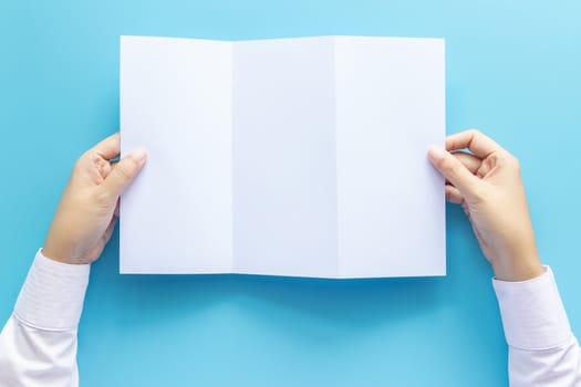 hand holding blank white paper for letter mock up, isolated on blue background with copy space. studio shot, horizontal