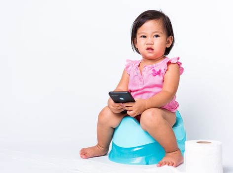 Asian little cute baby child girl education training to sitting on blue chamber pot or potty and play smart mobile phone with toilet paper rolls, studio shot isolated on white background, wc toilet