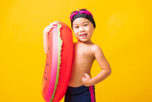 Summer vacation concept, Portrait Asian happy cute little child boy wear goggles and swimsuit hold watermelon inflatable ring, Kid having fun on summer vacation, studio shot isolated yellow background