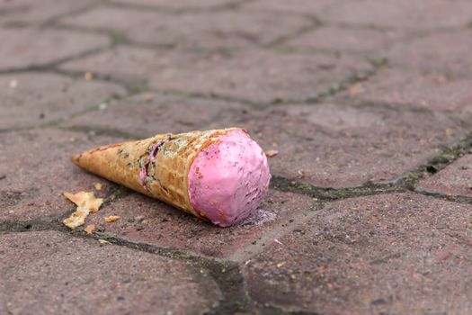 Strawberry ice cream falling on a street sidewalk and a broken waffle cone