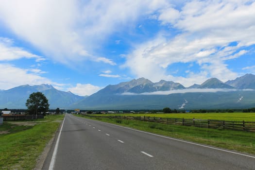 The road leading to the foot of the mountains past the green field