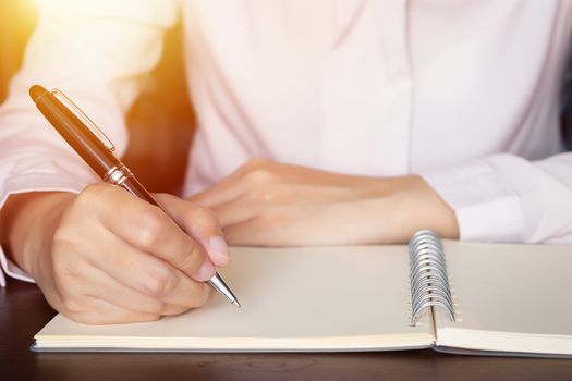 close up of business woman hands writing in spiral notepad on wooden table